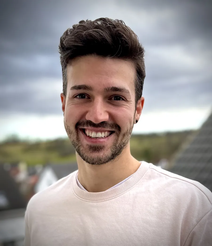 Dominik Jock lacht in die Kamera, im hellen Pullover, im Hintergrund Hausdächer