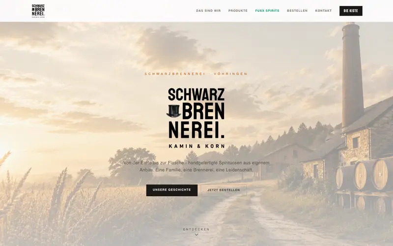 Startseite der Schwarzbrennerei Kamin & Korn: Logo vor einer Brennerei mit Schornstein im Abendlicht